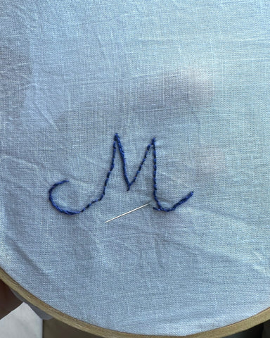 Letter M outlined in blue thread on white fabric - embroidery for monogram.