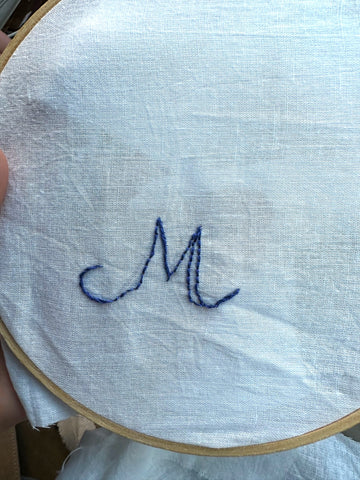 Monogram outline in blue thread on white fabric - letter M.