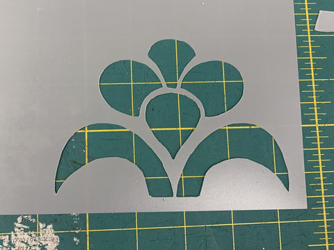 A floral design cut out of grey stencil paper on a green cutting mat.
