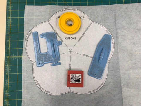 Using the bottom scalloped layer pattern piece for the biscuit cozy and cutting it out of interfacing in white on a green cutting mat.