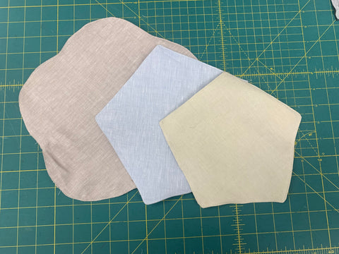 All three layers bottom layer made from beige linen, middle pentagon shaped layer made from light blue linen and top pentagon shaped layer made from light beige linen cotton blend fabric. on a green cutting mat.