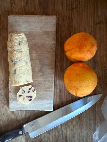 Roll of cookie dough on a wooden counter with a knife and two oranges