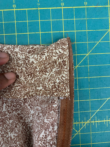 folded under half a inch on back waist facing and slipstitched to brown zipper, on a green cutting mat.