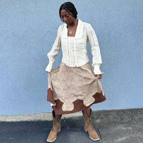 Woman twirling in a brown western skirt and cream blouse with cowboy boots on