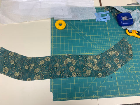 Teal and taupe hem flounce pieces sewn together on a green cutting mat.