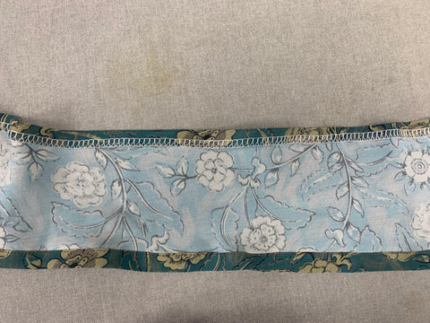 Wrong side of teal and taupe floral fabric, hemmed at the bottom of the hem flounce, serged at the top raw edge of the hem flounce and folded under 1/2"/1.6cm.