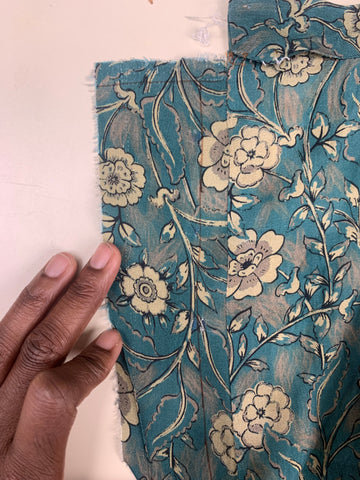 A drawn line 5/8"/1.6cm away from the seamline of facing D and the right-side skirt back B and a line 1/2"/1.3cm from the top short edge of facing D on teal and taupe floral fabric.