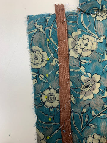 Pinned right side of the center of the zipper teeth onto the right side of the facing D. On teal and taupe floral fabric.