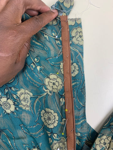 Left side of the zipper pinned to the placket E on the left side of back skirt B made from teal taupe floral fabric. With a hand on top of the piece.