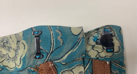 Attached black hook and eye to secure the waistband of skirt made from teal and taupe floral fabric.