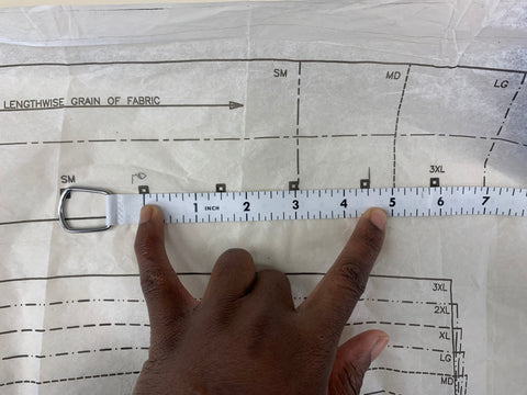 A tape measure, measuring 5 inches  from the square for size medium on the waistband pattern piece to the cutting line of size medium on waistband pattern piece. Fingers are place on the measurements.