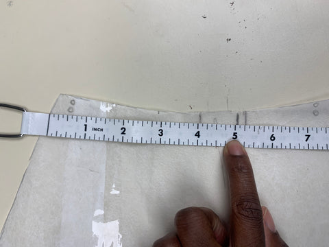 A tape measure, measuring 5 inches from the side of the back B pieces in towards the center back. On fabric tracing paper on a beige background.