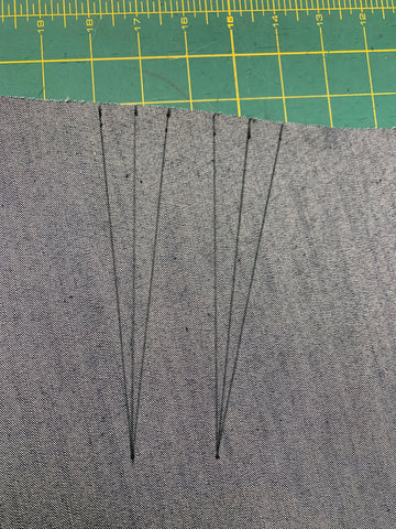 two darts drawn in black marker on the wrong side of denim fabric, on a green cutting mat.