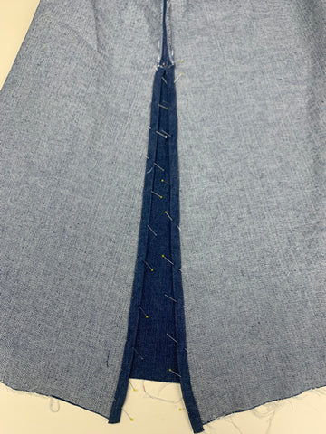 Pinned folded 1/2"/13mm to the wrong side of the denim fabric for the back slit on a grey background.