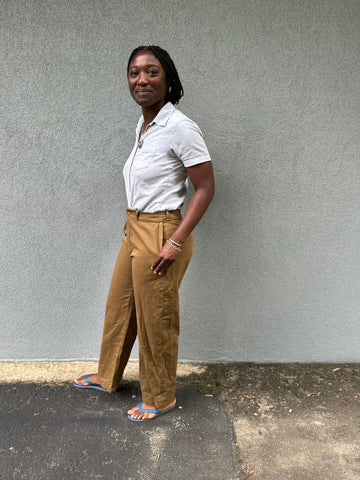 African woman standing sideways and smiling with hand in her olive khaki sanded twill pants in front on a grey wall.