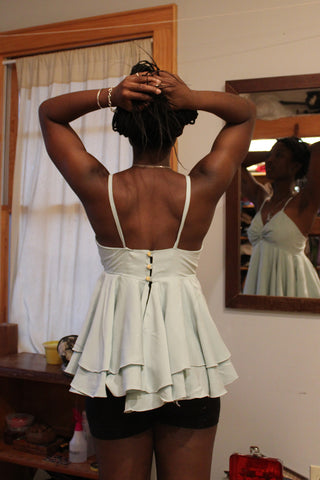 Back of model holding hair up while wearing garment  in a room with her front  reflected in the mirror in the background.