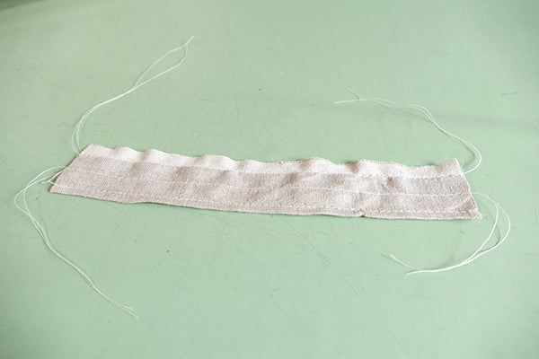 Strip of linen with gathering stitches and long tails.