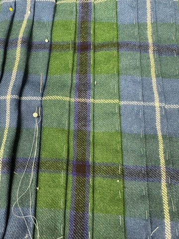 green and blue tartan fabric with pleats being basted by hand