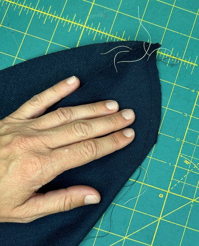 navy wool hat with dart sewn in it.  Hand on top of hat on the cutting mat