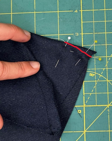 navy wool cloth with a red line marking where a dart will go, setting on a green cutting mat