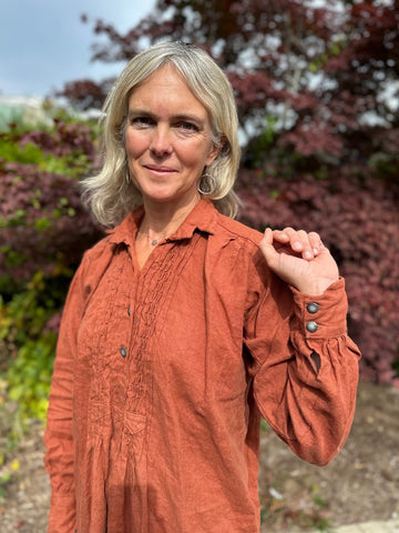 Top half of woman wearing a burnt orange linen dress, holding her hand up to show the sleeve placket.