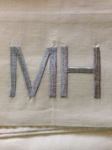 Block letter monogram - M H in grey on white fabric.