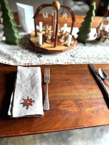 Napkin with poinsettia cross stitch set on wooden table with silverware and a table runner.