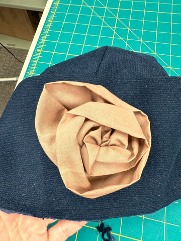 Pink cotton fabric flower sewn onto a navy blue hat.