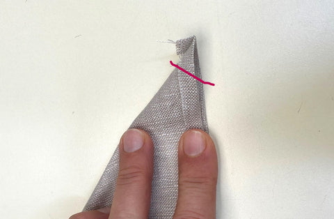 folded grey linen napkin at corners with a red line drawn at corner.