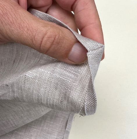 Grey linen napkin folded at corner to make a mitered corner.