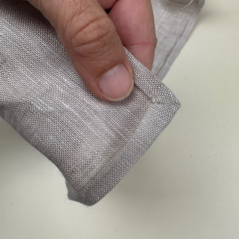 Grey linen napkin folded at corner to make a mitered corner.