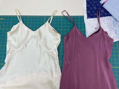 Two slip dresses are laid out flat on a table. There is a green cutting mat below them. There is a difference in the length of bust pieces between the two dresses.