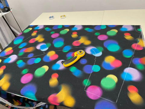 Fabric with colorful polka dots on a black background, laid out on the table to be cut into garment pieces