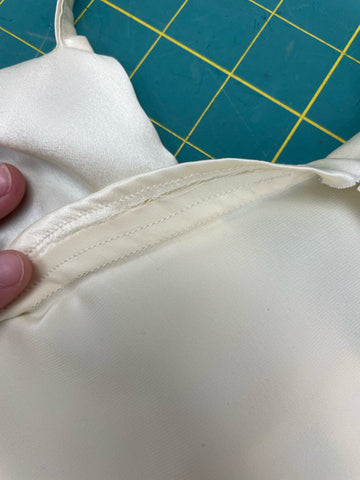 A slip dress has been turned inside out on a green cutting mat to show how the dress is constructed. A seam has been under-stitched where a facing meets the bodice of a dress.