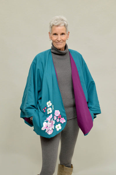Woman with short grey hair wearing an aqua short jacket with painted flowers on the front