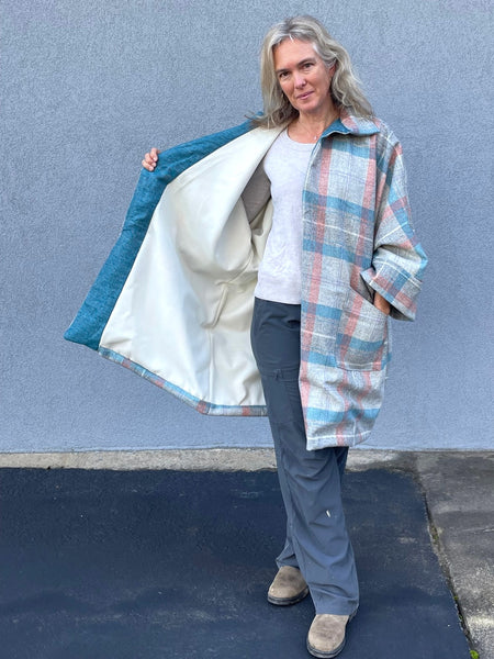Woman standing outside by a grey wall in a plaid overcoat, showing the white inside lining