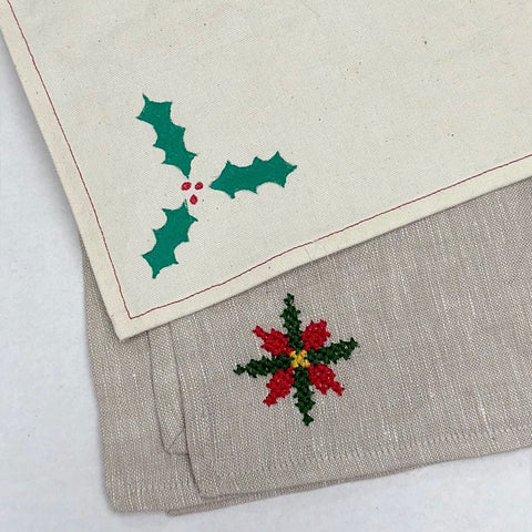 two cream colored napkins with embroidery and fabric paint in holiday motifs.