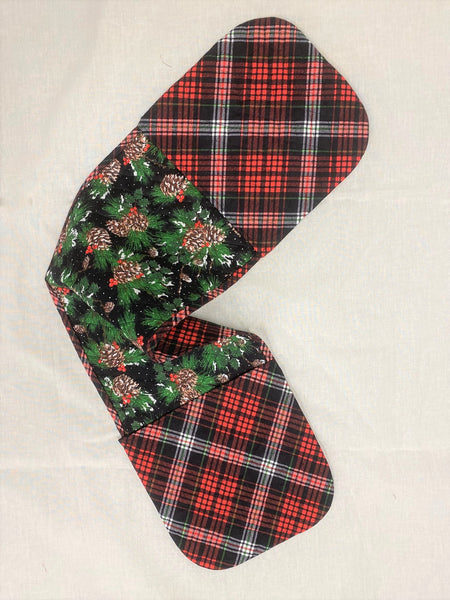 Oven mitt with red and green christmas fabric laying on white fabric.