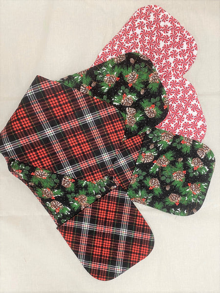 Three Christmas fabric oven mitts laying on a white fabric.