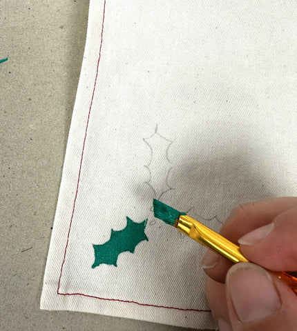 Painting the holly leaf green with paint brush in photo.