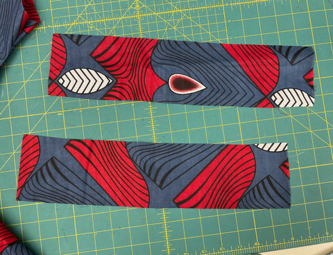 two strips of red and blue fabric for cuffs on a green cutting mat