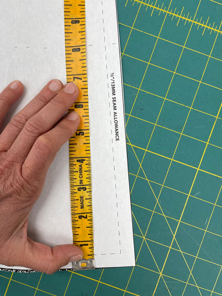 white pattern piece on a green measuring board with a yellow measuring tape held by a hand at 8 inches.
