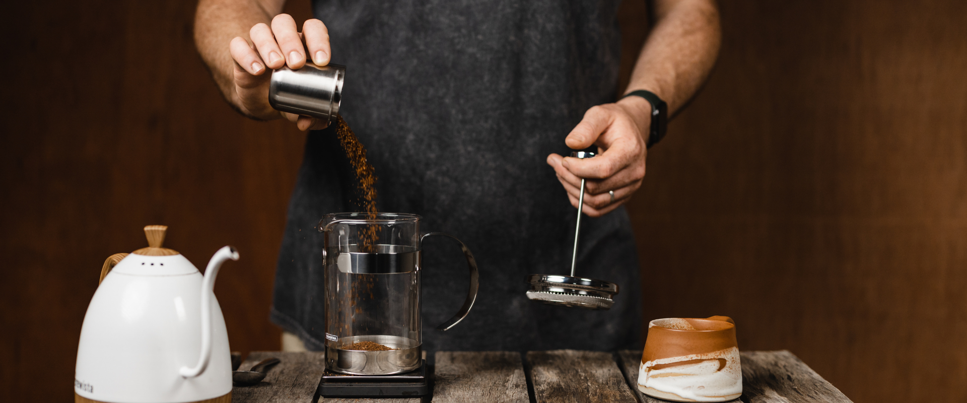 person pouring ground coffee into plunger