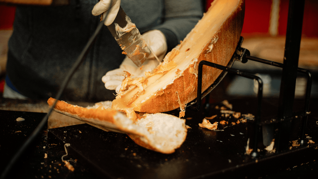 Raclette being scraped onto a baguette