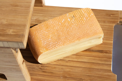 rectangular piece of washed rind cheese on wooden board against white background