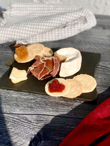 black cheese board with french camembert cheese, crackers, charcuterie, and jam on table