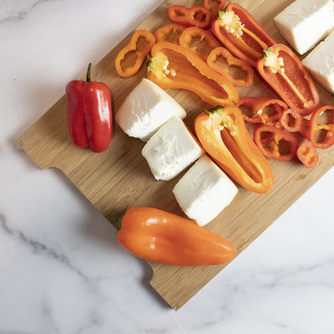 overhead view of small bamboo cheese board with white cheese and red and orange sweet peppers