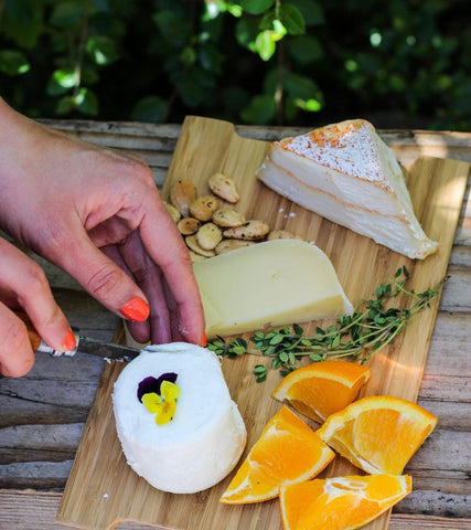 bamboo cheese server with oranges, soft cheese, herbs, and hands on table