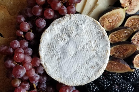 overhead closeup of wheel of french camembert cheese with grapes and figs