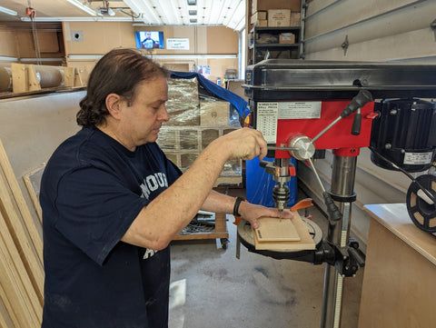 woodworker in wood shop uses a drill press to make holes in the back panel of wooden cheese grotto 